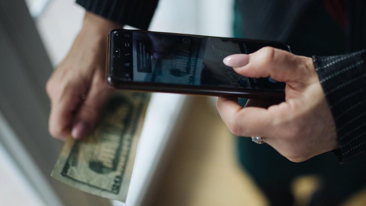 Hands holding a $50 bill and a smartphone