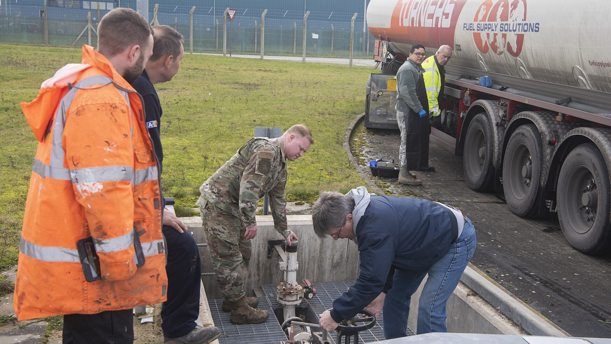 Personnel work a fuel valve beside a fuel supply tanker