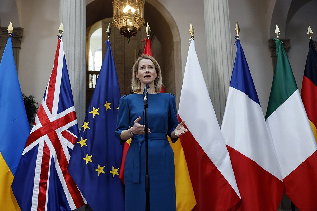 Kaja Kallas speaking at a microphone in front of European flags